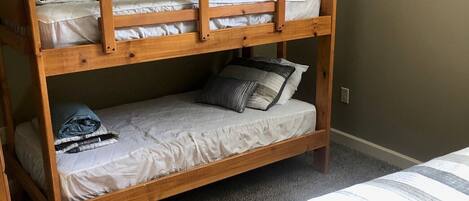 A bunk bed with two levels, a carpeted floor, and a plain wall.
