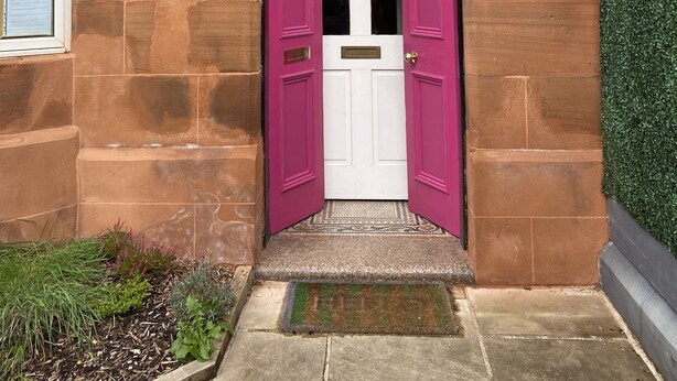 A traditional stone building with a numbered entrance, a white door, and a small step leading up to it.