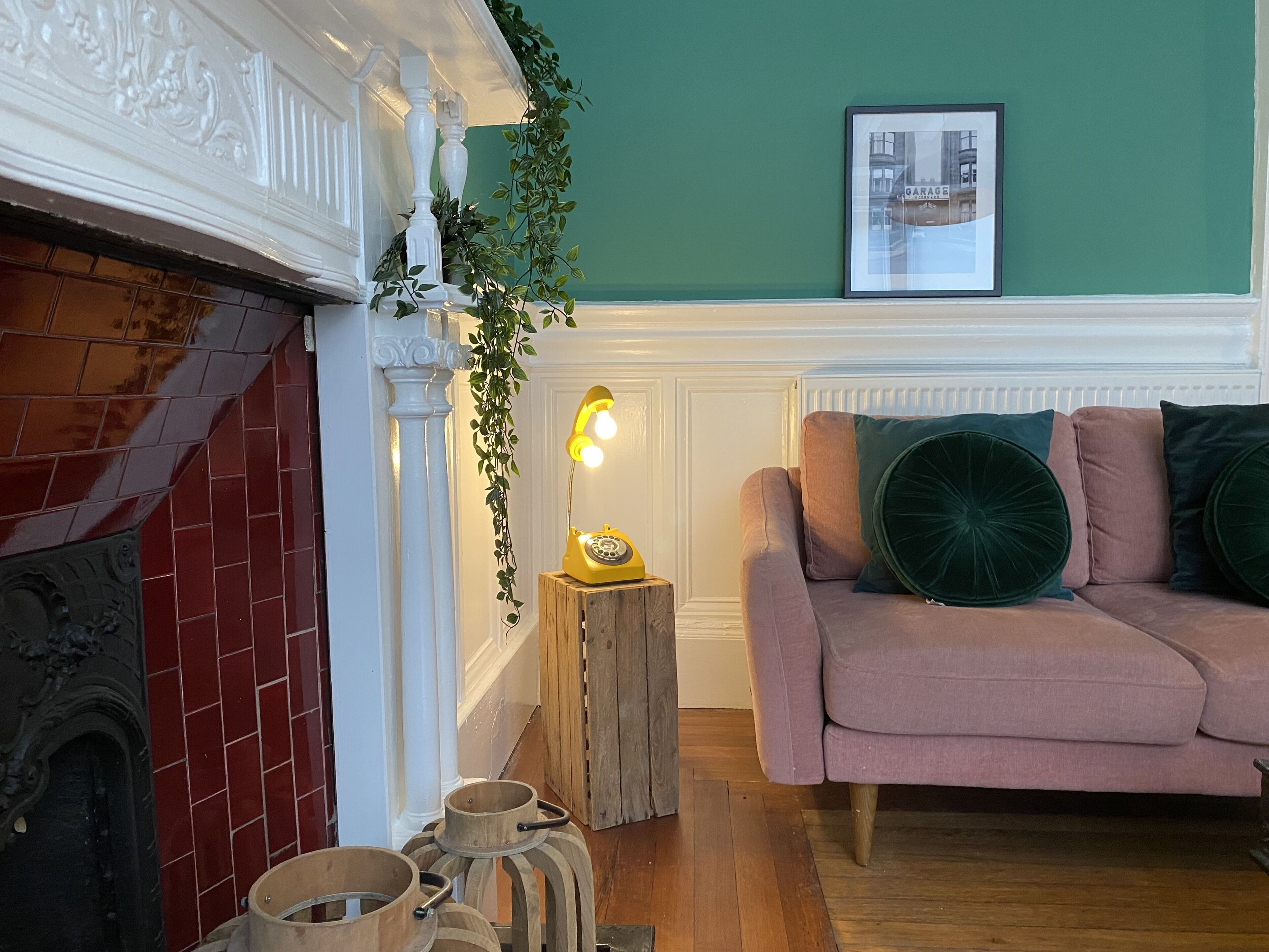 A cozy living room with a fireplace, a sofa with cushions, a wooden side table, and a framed picture on the wall.