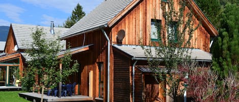 A wooden cabin with a sloped roof, a porch with chairs, and a small deck area.