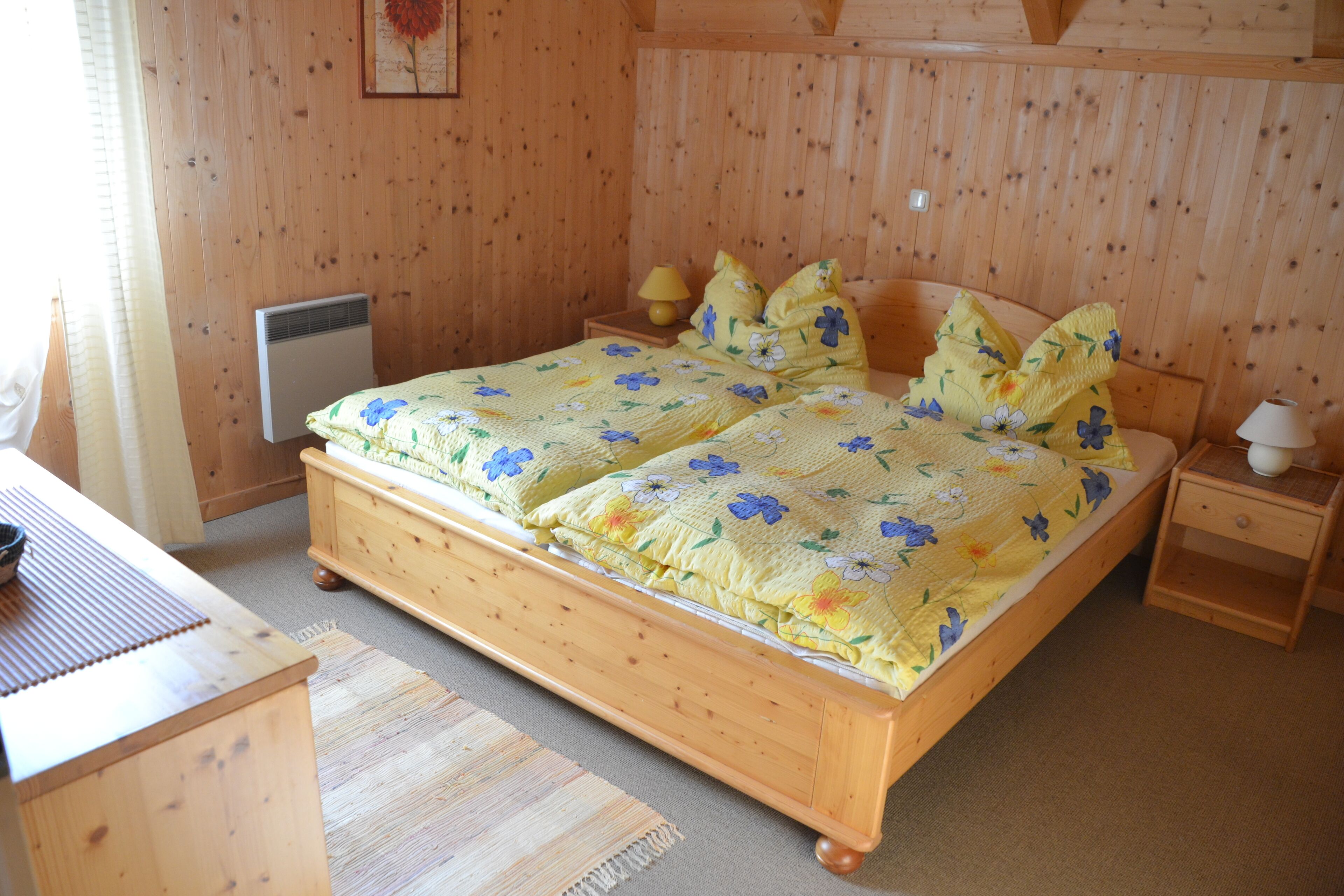 A wooden bed with floral bedding, a bedside table with a lamp, and a wooden nightstand.
