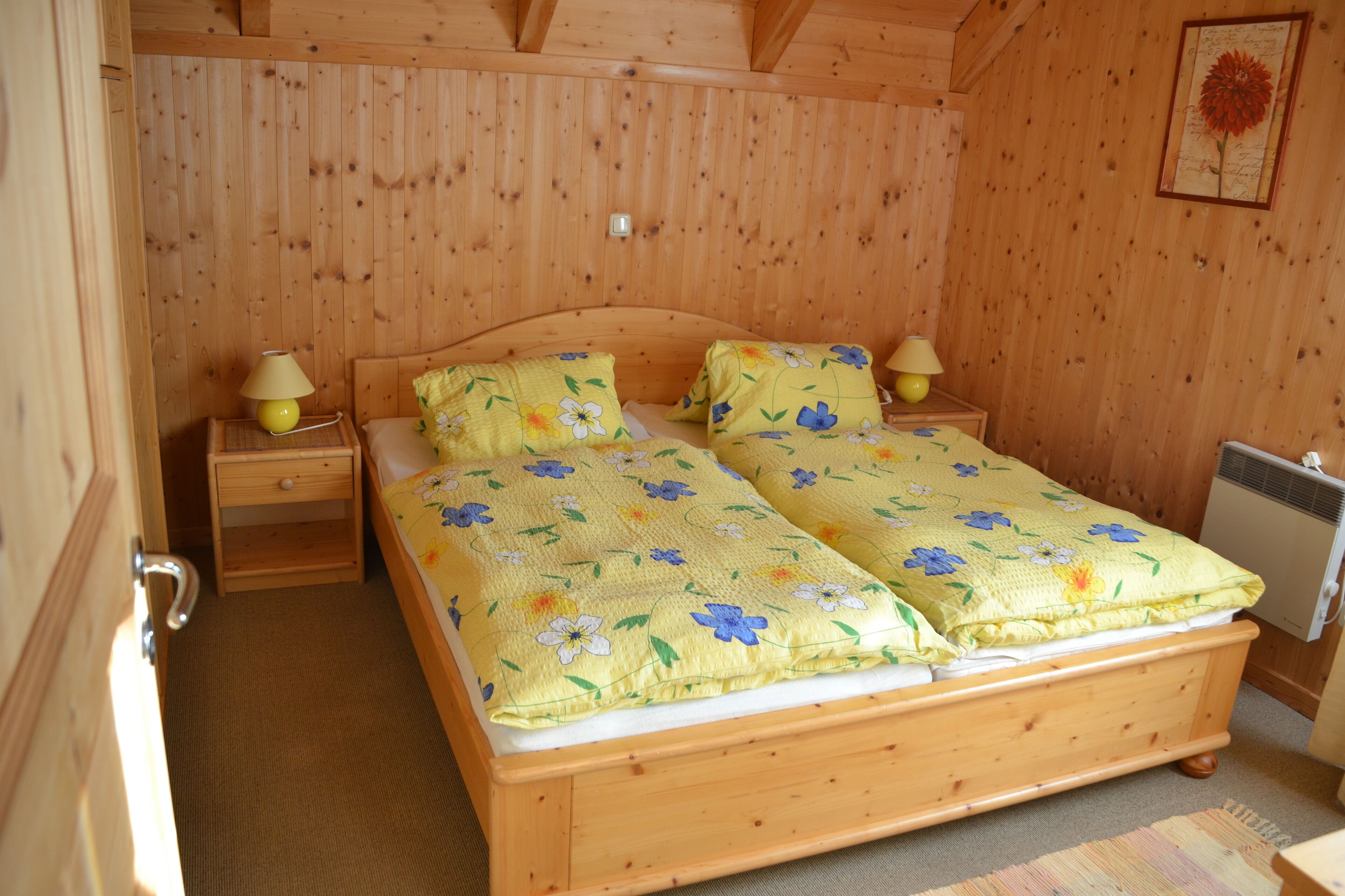 Una habitación de madera con una cama doble, dos mesitas de noche y un radiador.