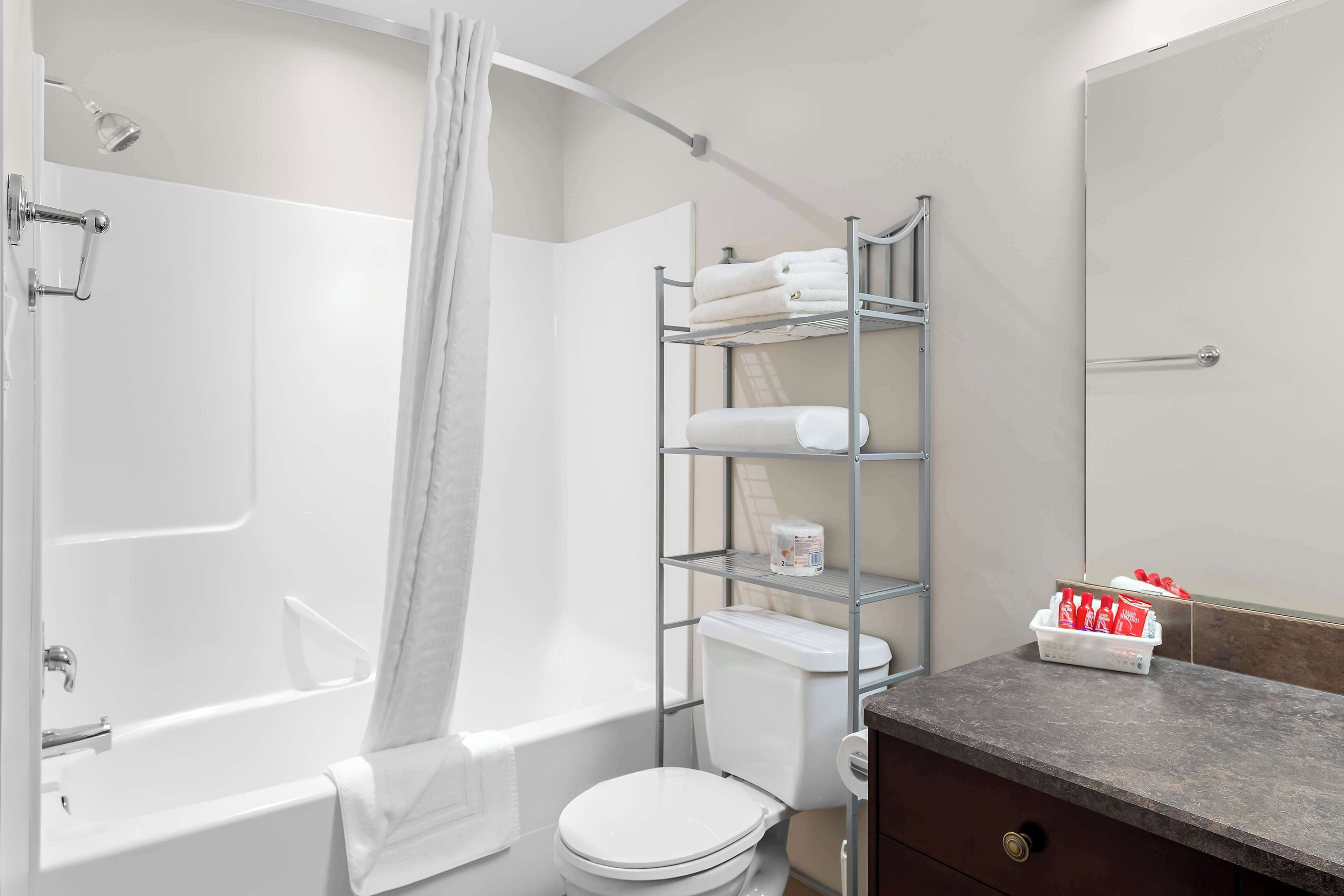 A bathroom with a bathtub, toilet, and a shelf with toiletries.
