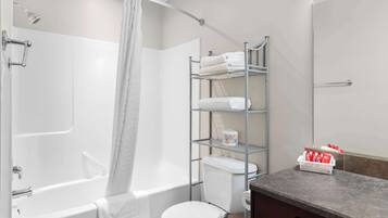 A bathroom with a bathtub, toilet, and a shelf with toiletries.
