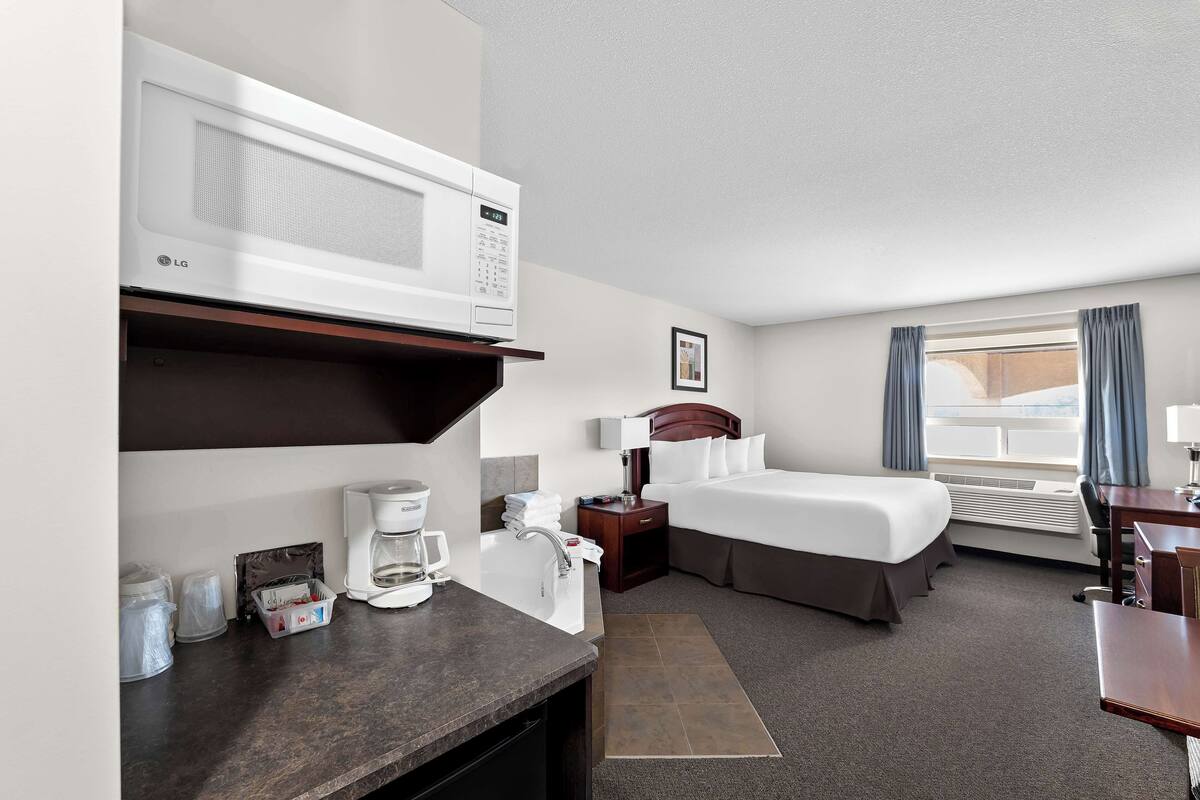 A hotel room with a bed, a desk, a microwave, a coffee maker, and a bathroom with a sink and toilet.