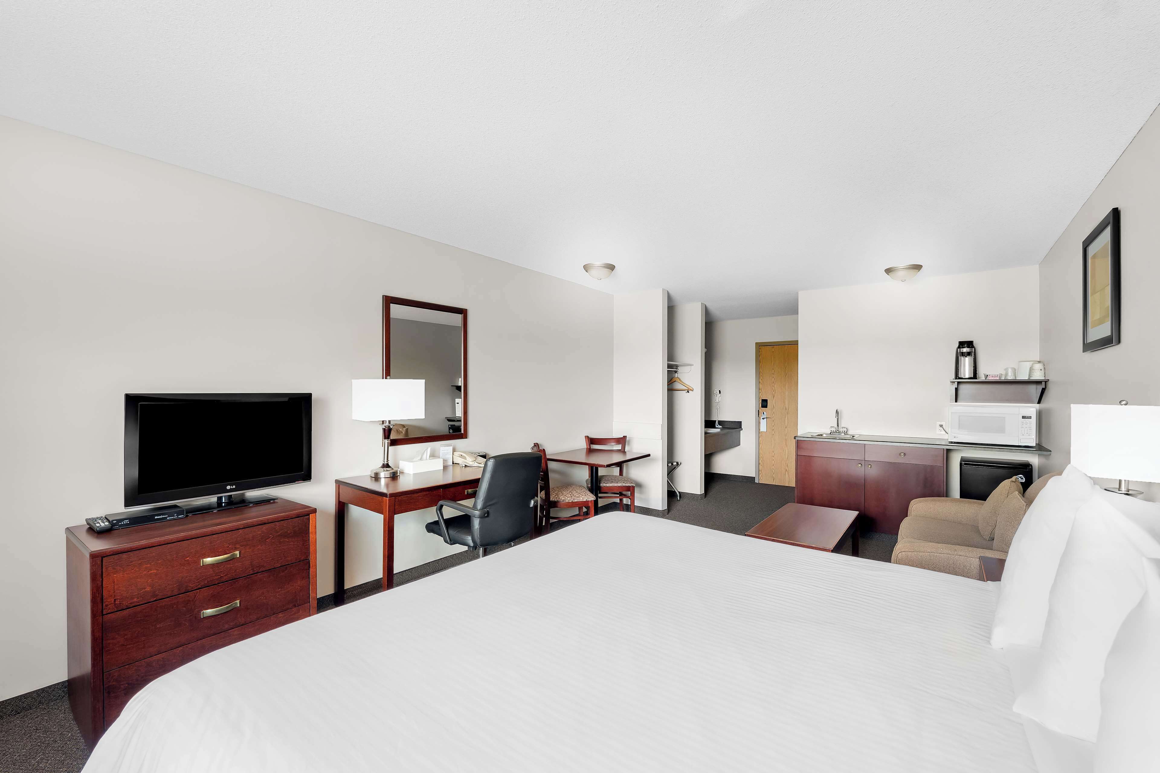 A hotel room with a bed, a desk with a computer, a TV, a chair, a dresser, a microwave, and a coffee maker.