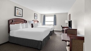 Ett hotellrum med två sängar, ett skrivbord, en stol, en TV och ett fönster med gardiner.