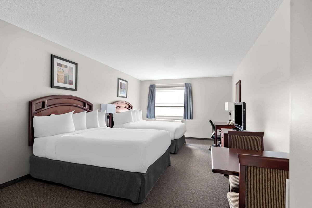 A hotel room with two beds, a desk, a chair, a TV, and a window with curtains.