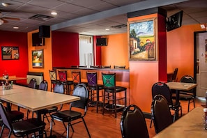 A restaurant interior with tables and chairs, a painting on the wall, and a window with curtains.