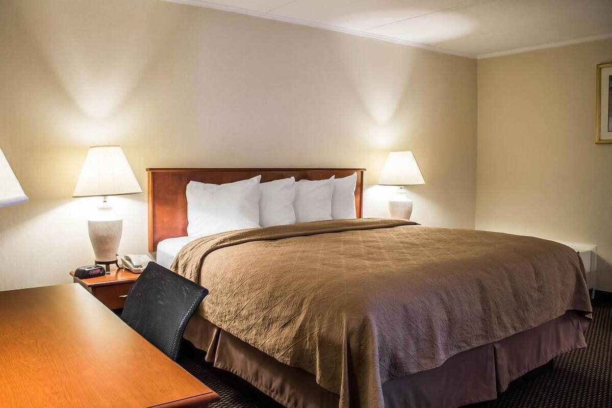 Habitación de hotel con una cama, dos lámparas de noche, una mesita de noche de madera, un teléfono y un escritorio con una silla.