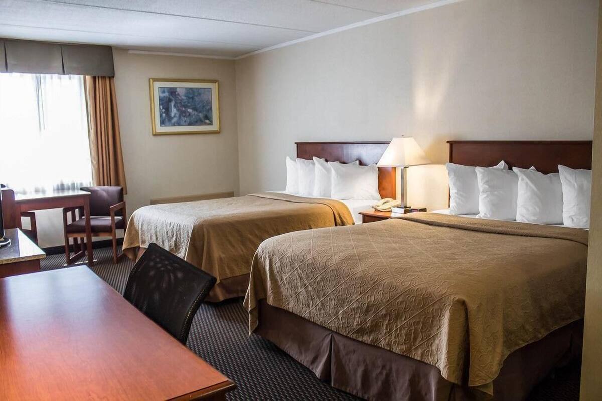 Habitación de hotel con dos camas, un escritorio, una silla, una lámpara y un cuadro en la pared.