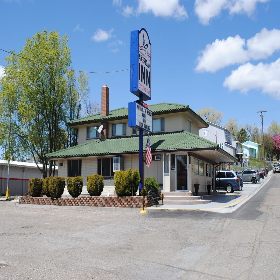 A two-story motel with a green roof, a signboard, and a small parking area.