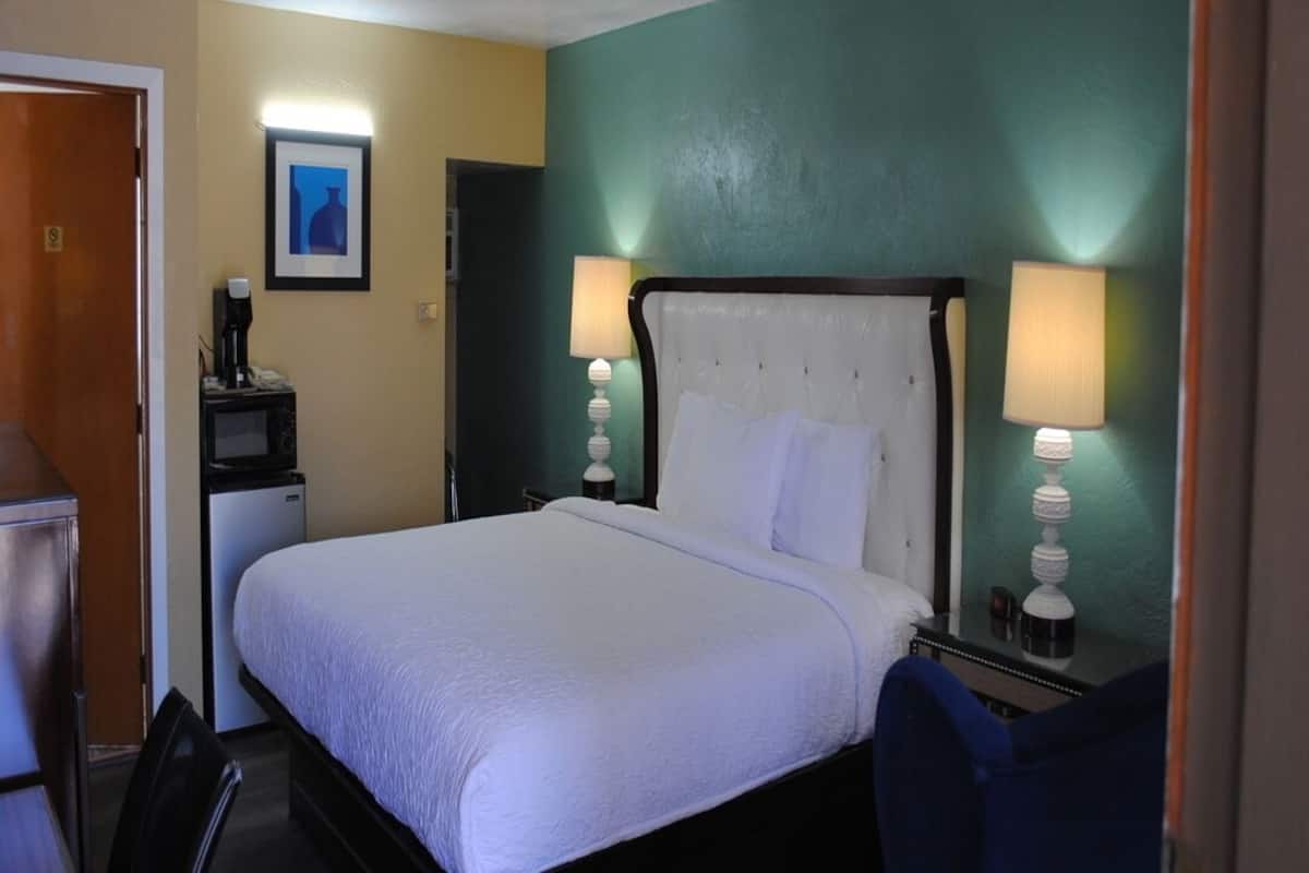 A hotel room with a bed, bedside lamps, a desk with a coffee maker, and a small refrigerator.