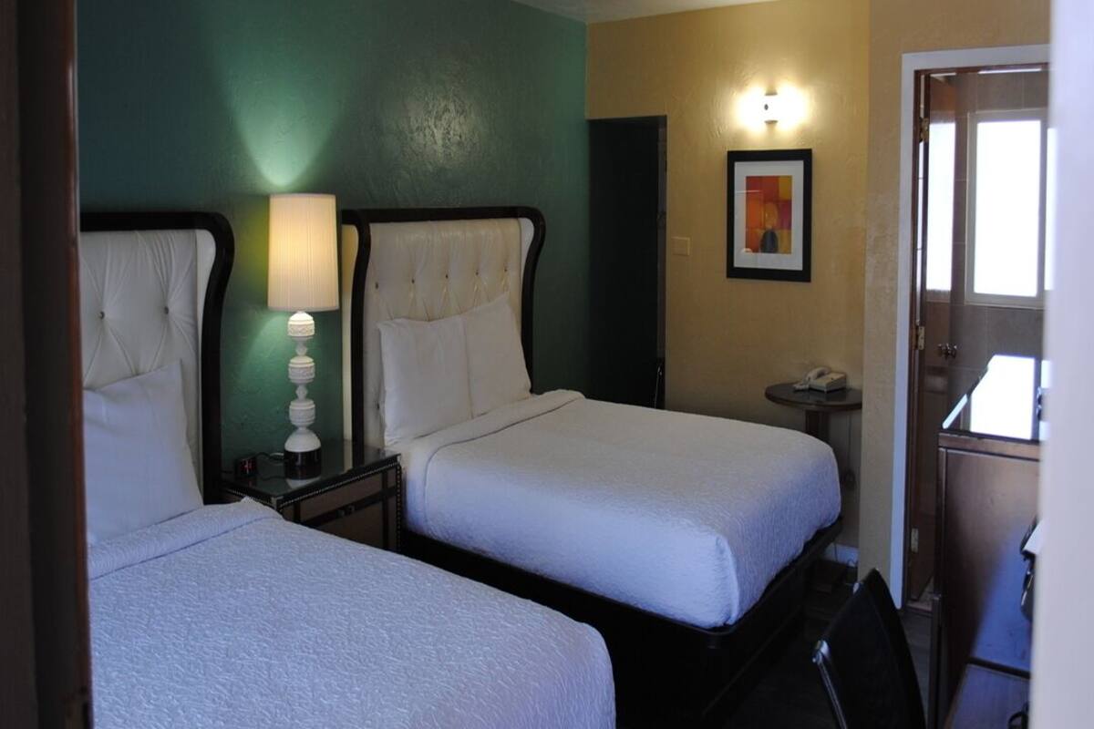 A hotel room with two beds, a desk, a chair, a lamp, and a painting on the wall.