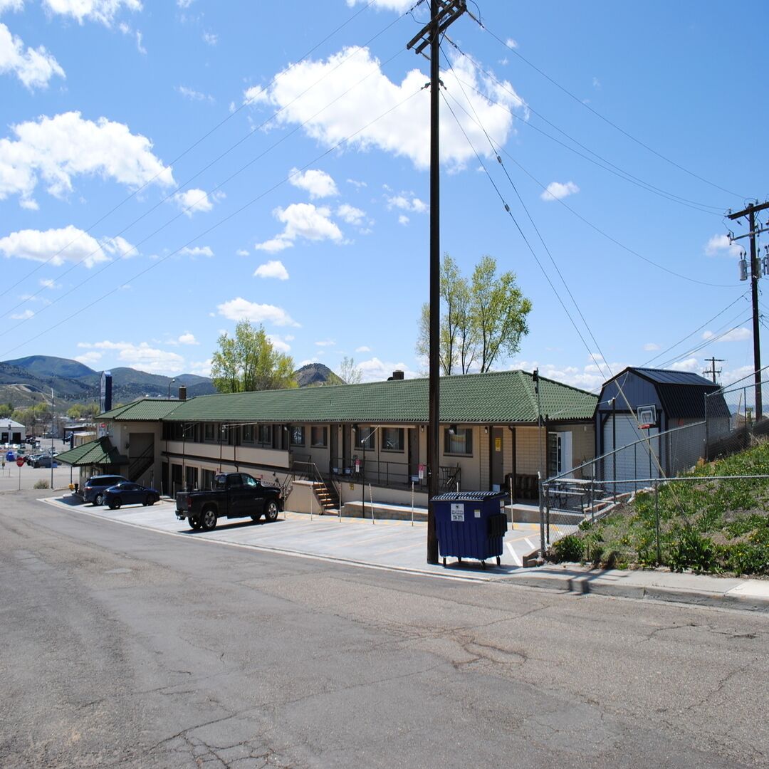 Un motel con techo verde, zona de estacionamiento cubierta y una pequeña cancha de baloncesto.