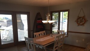 Un comedor con mesa y sillas de madera, una tabla de surf y un adorno de pared con temática náutica.