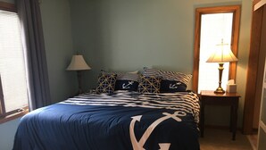 Un dormitorio con cama, mesita de noche, lámpara y ventana con cortinas.