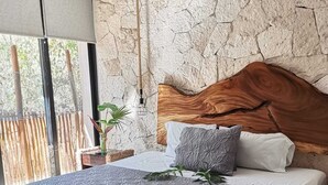 Een moderne slaapkamer met een stenen muur, een houten hoofdbord en een groot bed met grijze beddengoed.