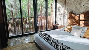 Een slaapkamer met een groot bed, een stenen muur en uitzicht op een bamboombordes door een glazen deur.