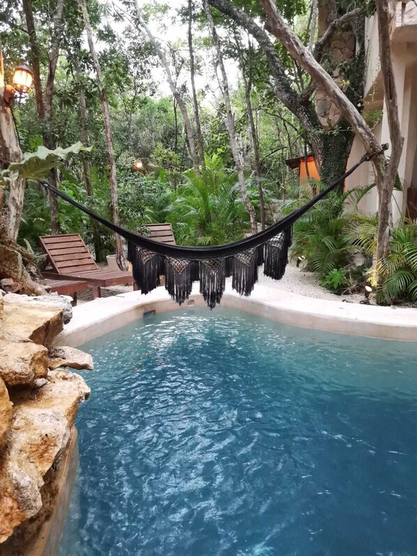 A hammock over a pool surrounded by lush greenery and a stone wall.