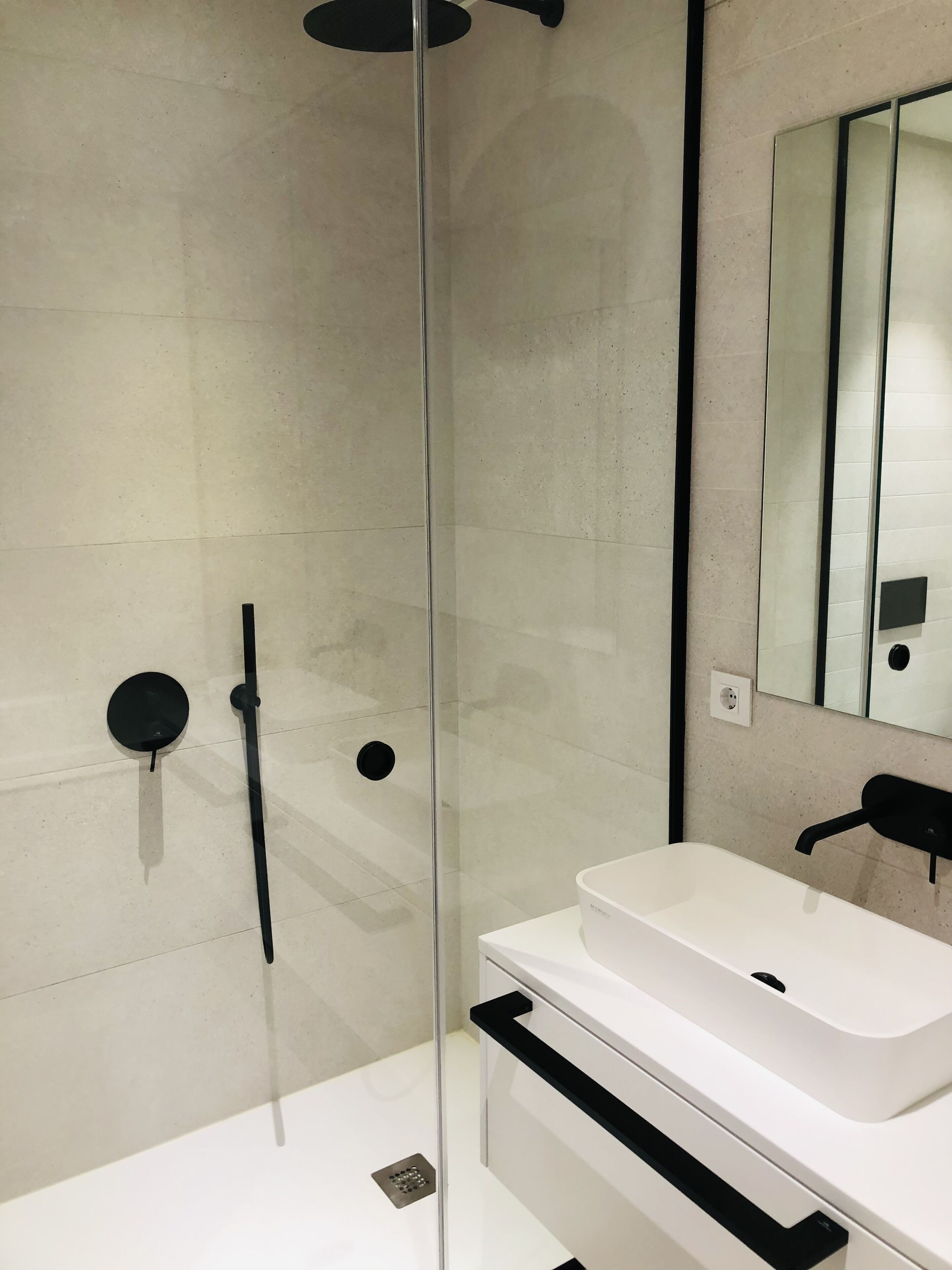 Un baño moderno con cabina de ducha de vidrio, un lavamanos blanco y un espejo grande.