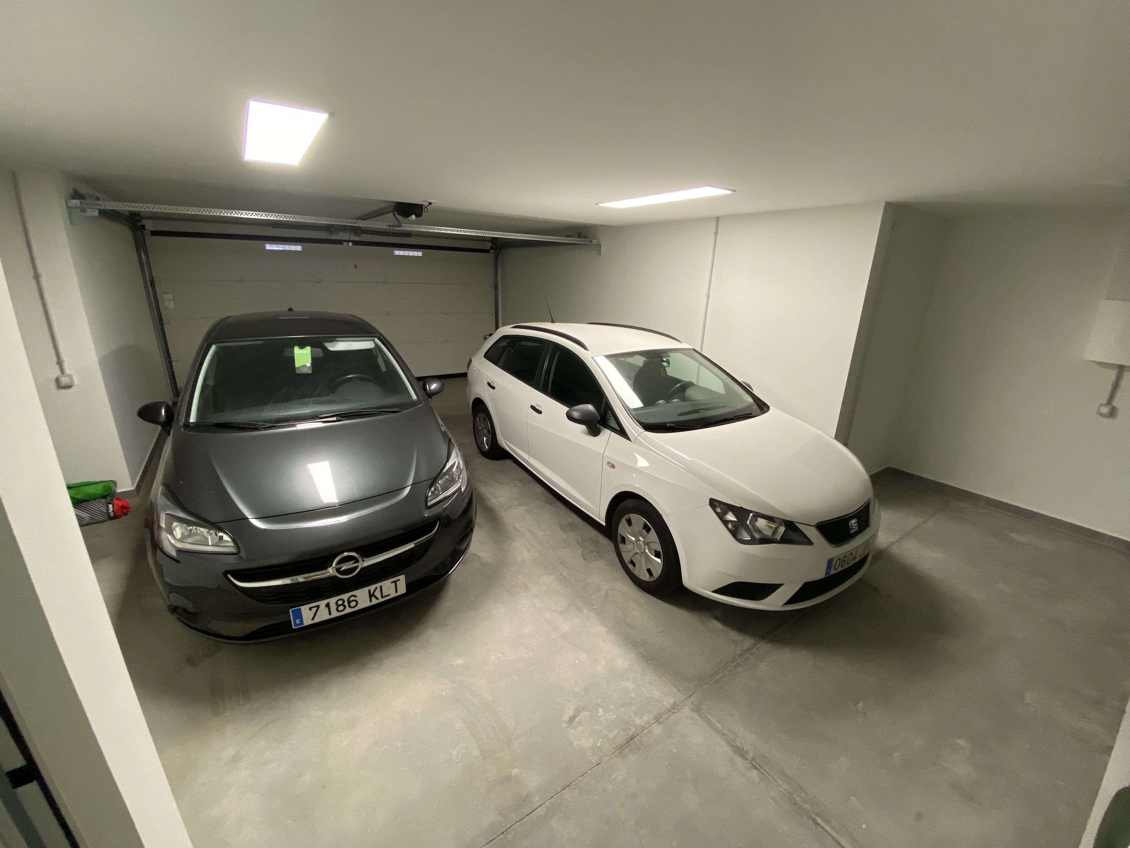 Two cars parked in a garage with a concrete floor and white walls.