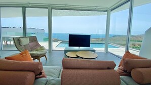 Een moderne woonkamer met een grote televisie, comfortabele zitplaatsen en uitzicht op de oceaan.