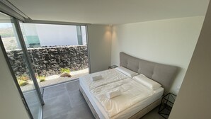 Een moderne slaapkamer met een groot bed, uitzicht op een rotsachtig landschap door een glazen deur, en een balkon met een stenen muur.