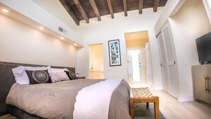 Een slaapkamer met een bed, een houten bankje, een kledingkast en een deur naar een andere kamer.
