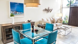 Een moderne woonkamer met een glazen eettafel, blauwe stoelen, een bank en een salontafel.