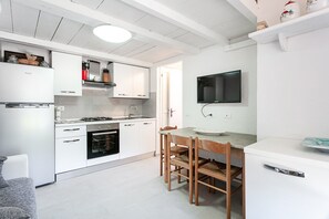 Una cucina moderna con mobili bianchi, forno integrato, tavolo da pranzo con sedie e televisore piatto montato a parete.