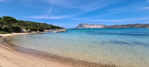Una playa con agua cristalina, un promontorio rocoso y montañas al fondo.