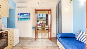 A room with a bed, a desk, a kitchen area, and a view of a balcony. - Holiday Apartment "Bilocale Geranium Beach" with Terrace & Air Conditioning (San teodoro)