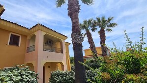A two-story building with a balcony, surrounded by palm trees and greenery. - Holiday Apartment "Bilocale Geranium Beach" with Terrace & Air Conditioning (San teodoro)