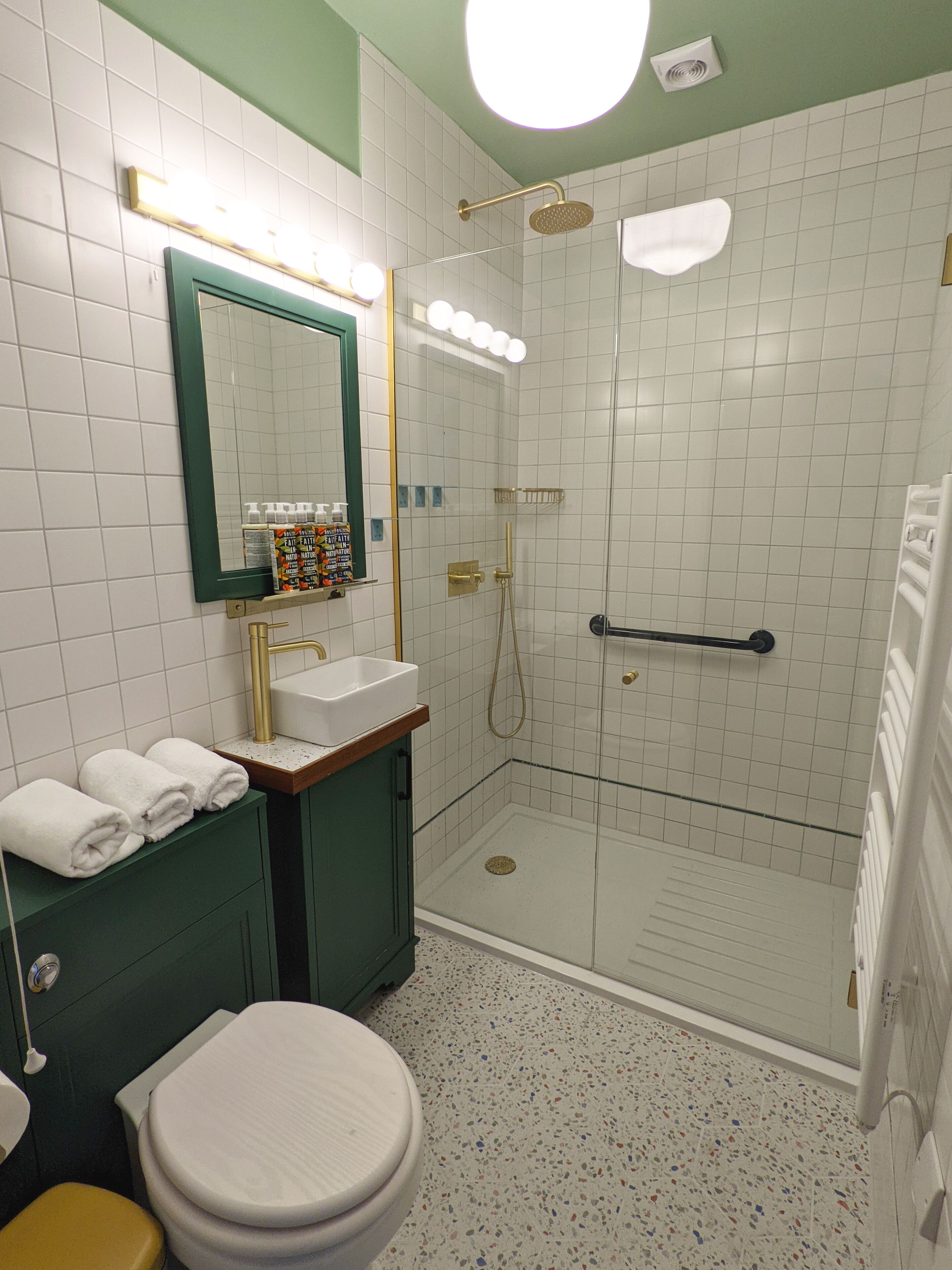A bathroom with a glass-enclosed shower, a sink with a gold faucet, a mirror with lights, and a toilet.