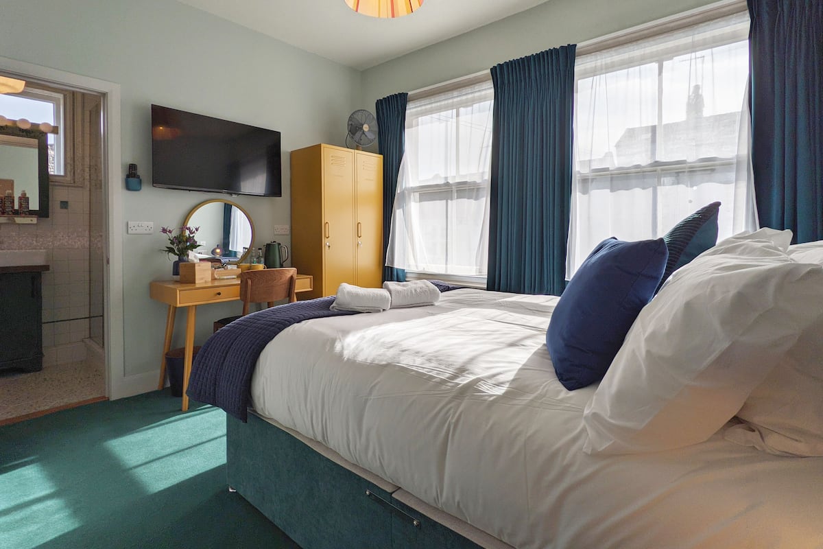 A hotel room with a bed, a desk with a chair, a wardrobe, a television, and a window with curtains.