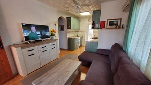 Een woonkamer met een bank, een salontafel, een televisie en een keuken op de achtergrond.