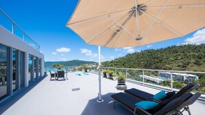 Eine Dachterrasse mit einer großen Sonnenschirm, Liegestühlen und Kübelpflanzen.