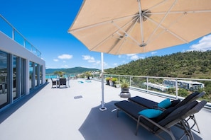 A rooftop terrace with a large umbrella, lounge chairs, and potted plants. - Ocean Dreams Whitsunday (Airlie Beach)