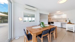 Eine moderne Küche mit weißen Schränken, einem Holztisch und Blick durch ein großes Fenster.