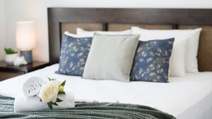 Ein ordentlich bezogenes Bett mit einer grünen Decke, einem weißen Kopfkissen und einem blau gemusterten Kissen.