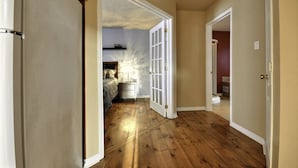 A hallway with wooden flooring leading to a bedroom with a bed and a nightstand.