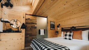 A wooden cabin bedroom with a bed, a mirror, a fan, and a door leading to a bathroom. - Blue Buffalo Resort (Island Park)