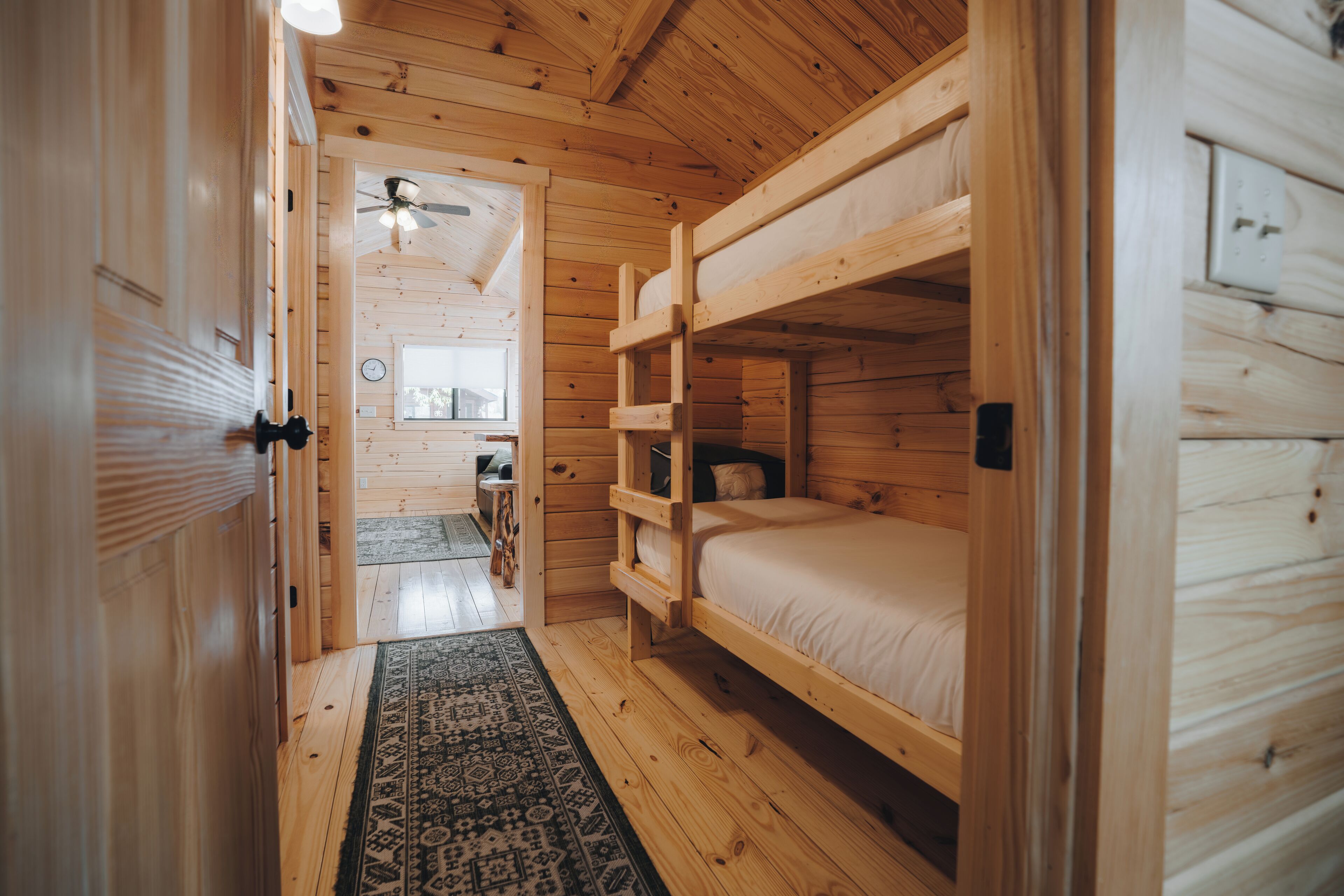 A wooden cabin with bunk beds, a ceiling fan, and a rug.