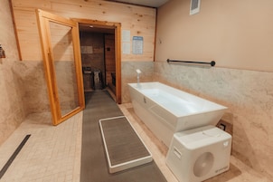 Un cuarto de sauna con puerta de madera, una bañera blanca, un tapete y un calentador de sauna.