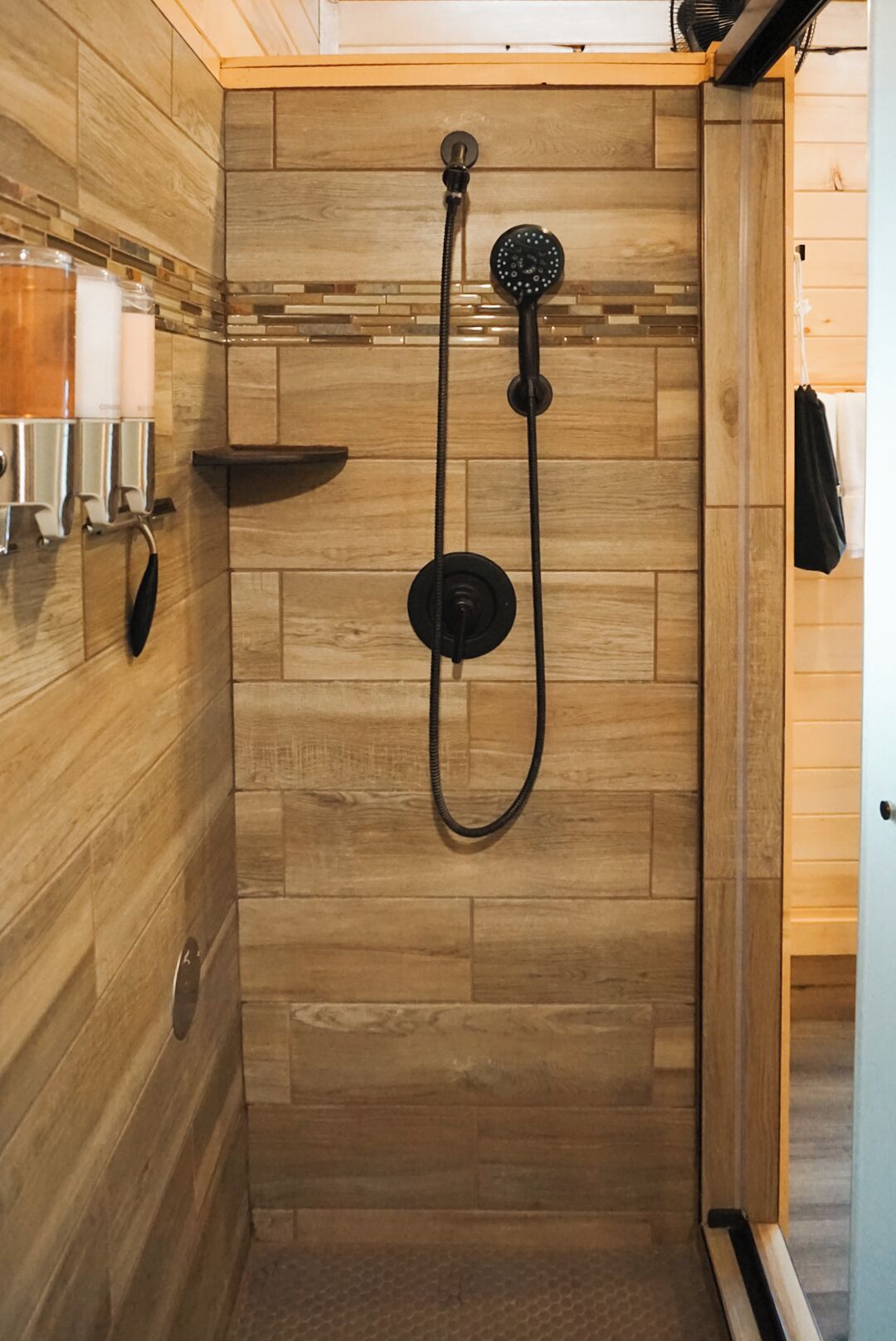 A wooden-paneled shower enclosure with a handheld showerhead and a fixed wall-mounted showerhead.