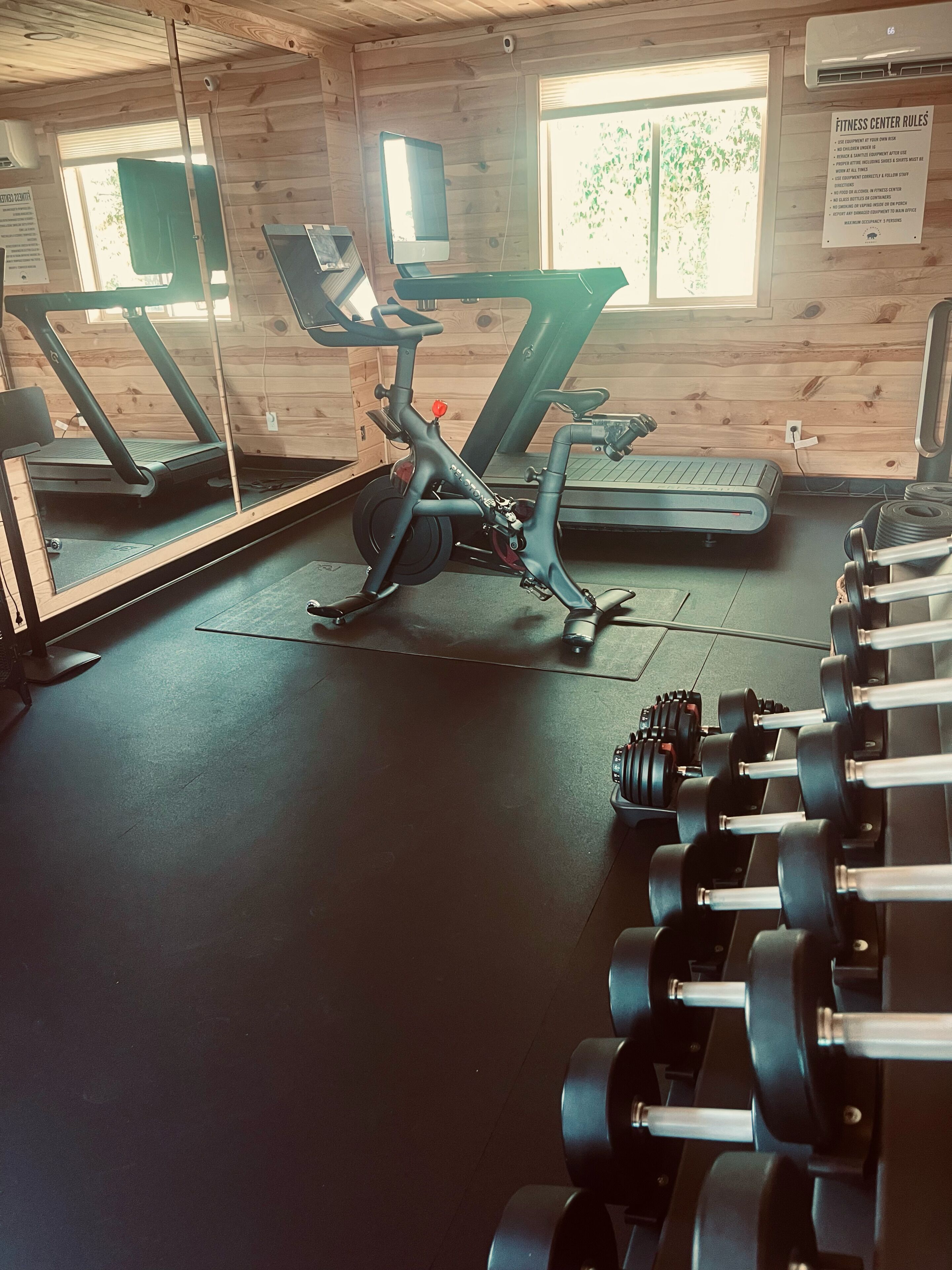 Un gimnasio con equipo de ejercicio, incluyendo cintas de correr y una bicicleta estática, además de un estante con mancuernas.