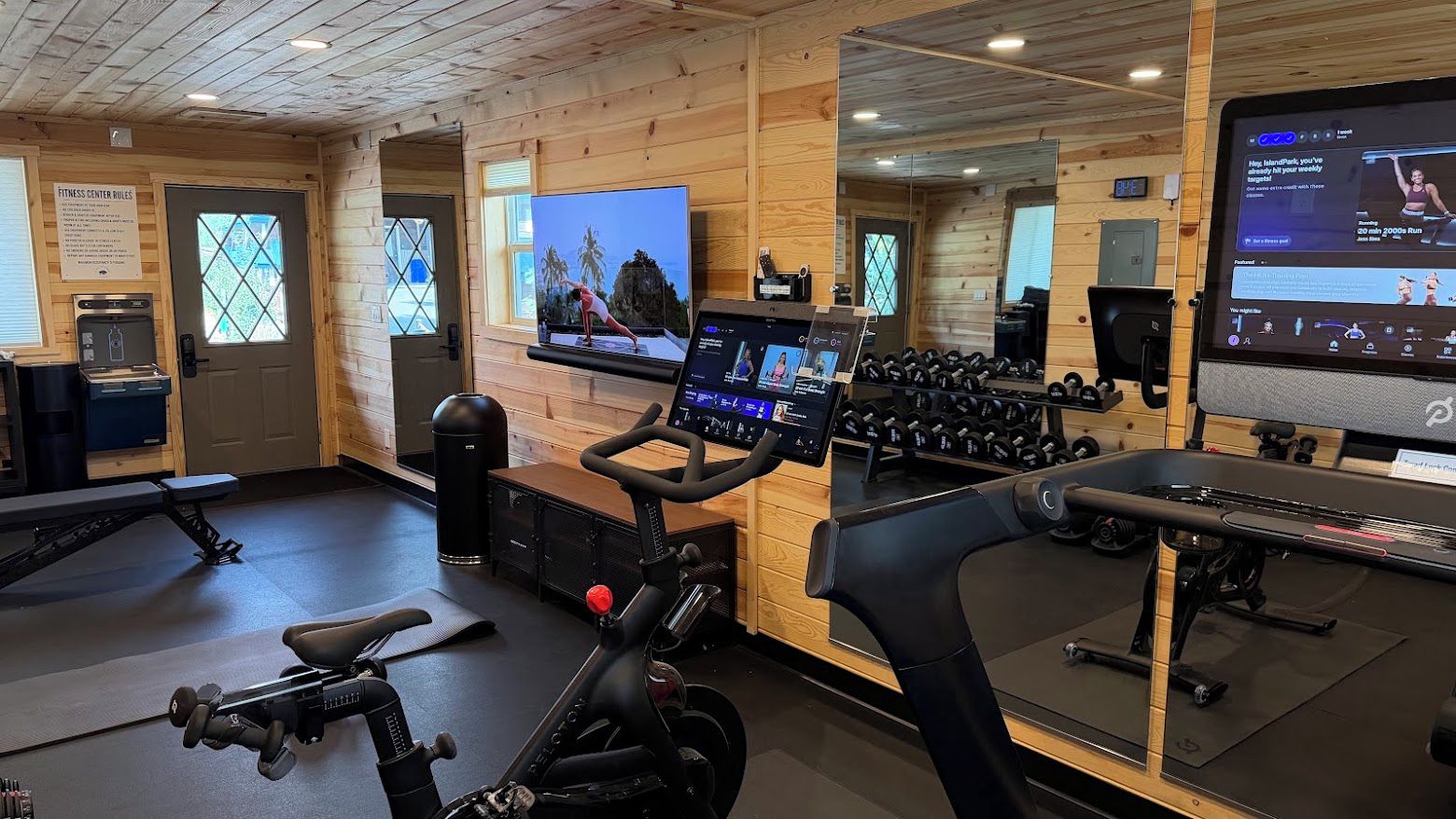 A gym with exercise bikes, a treadmill, and a TV screen displaying workout videos.
