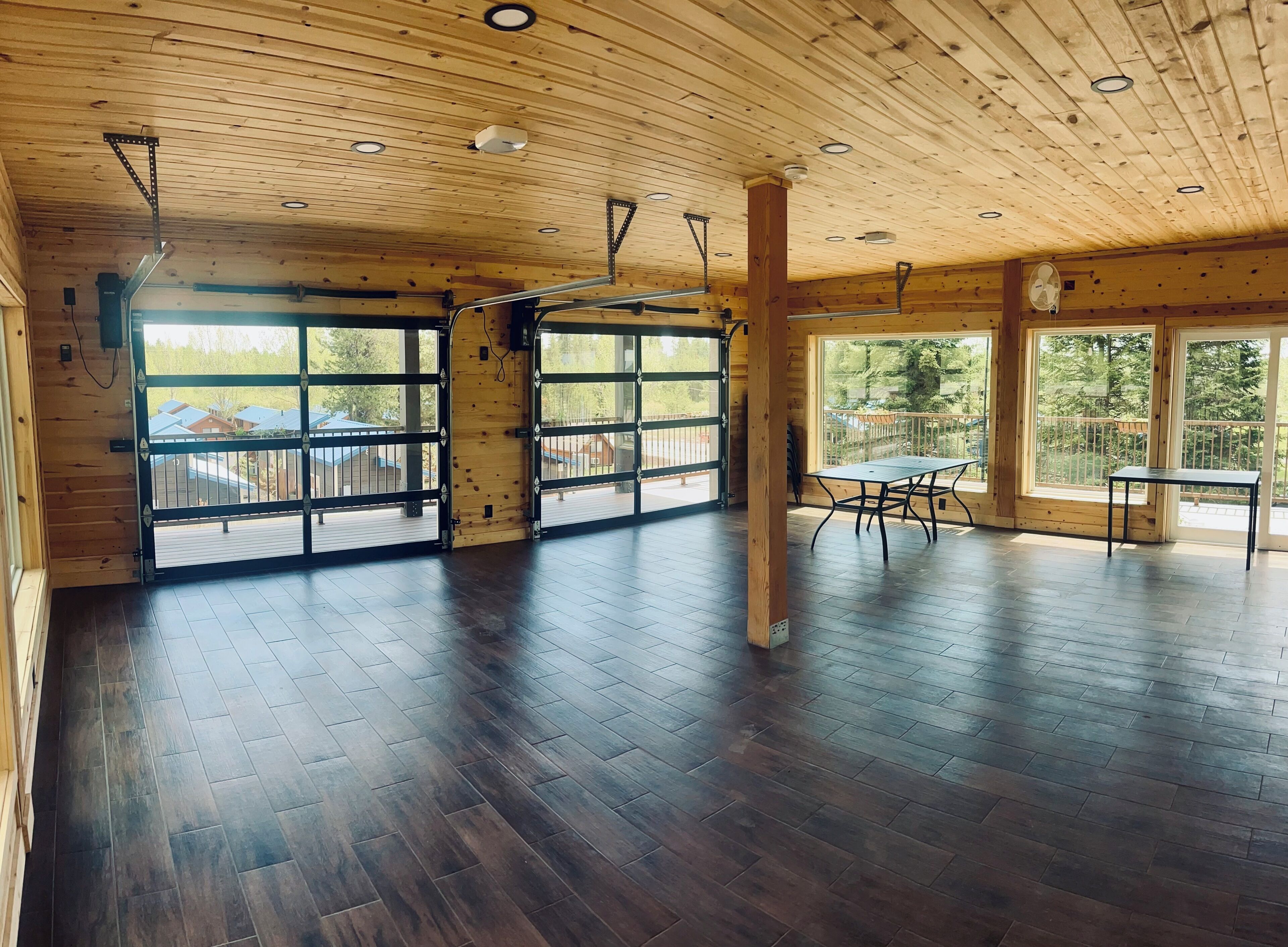 A spacious room with a wooden ceiling, large windows, and a table with chairs.