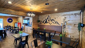A restaurant with wooden walls, black metal chairs, and tables. There is a mountain mural on the wall and a Coca-Cola sign. - Blue Buffalo Resort (Island Park)